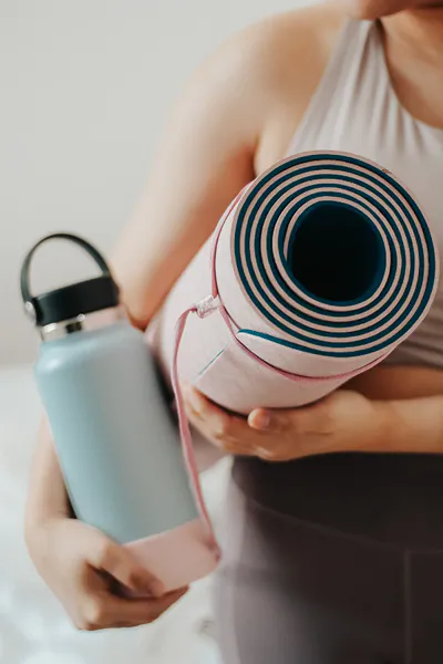 Image of a person with a yoga mat and a water bottle, engaging in physical activity to increase her overall wellbeing and feel balanced